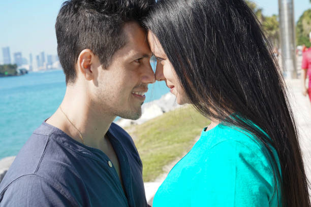 Latin american couple leaning their foreheads together smiling while standing outside