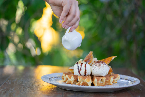Hand pouring maple syrup on fresh waffles with ice cream on a wooden background