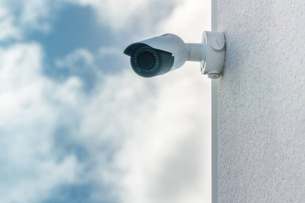 CCTV security camera in front blue sky background installed on white building wall stock photo