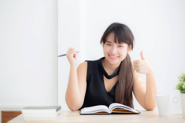 istock Beautiful portrait young asian woman smiling sitting study and learning writing notebook and diary in the living room at home, girl homework, business woman working on table, education concept. 1144426973