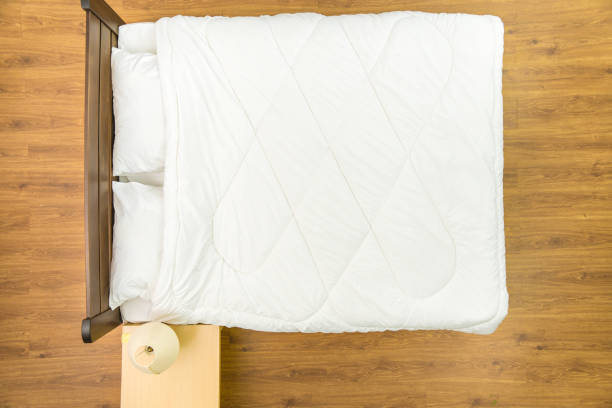 Unmade bed of white linens pillows and blanket.