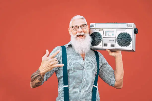 Photo of Happy senior man listening to music with boombox outdoor - Crazy hipster male having fun dancing with vintage stereo - Concept of elderly people lifestyle