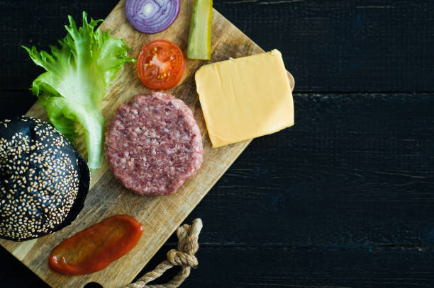 istock Ingredients for black Burger on wooden chopping Board, black background. 1144430366