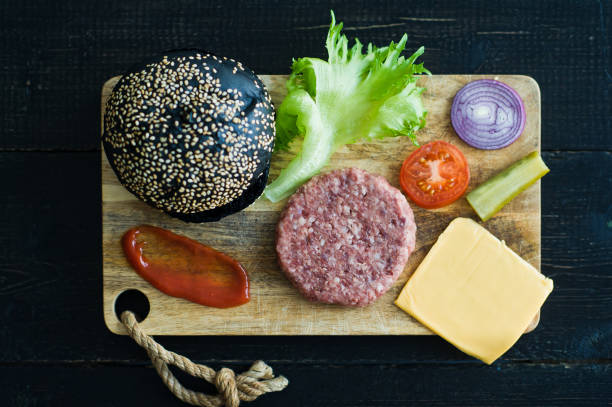 istock Ingredients for black Burger on wooden chopping Board, black background. 1144430375