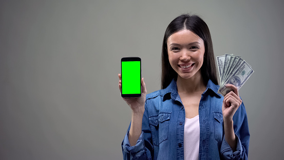 Young asian woman holding smartphone and dollars, IT application development