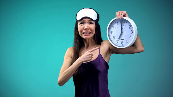 Frustrated girl pointing at 7 am on clock face, overslept and getting late