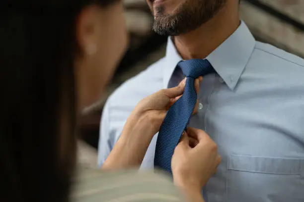 Close up of loving woman helping partner with his necktie both smiling