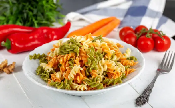 Multicolored pasta with vegetable on wooden background ve vegetables