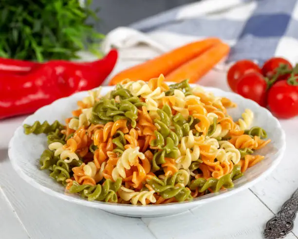 Photo of Multicolored pasta with vegetable on wooden background ve vegetables