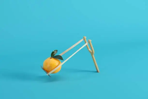 Photo of Orange in a slingshot on blue background. Minimal fruit idea concept.