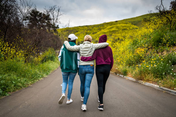 madre e figlie che camminano verso il campo fiorito - rear view women back back of head foto e immagini stock