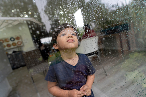 Cute little boy looking out the window on a rainy day very sad