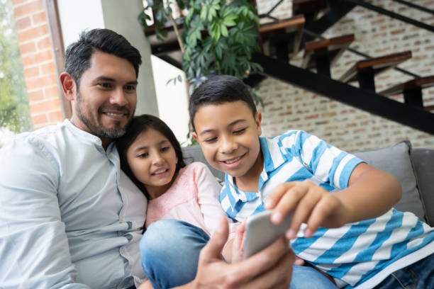 istock Loving father relacing on couch with daughter and son while they play with a smartphone 1144447607