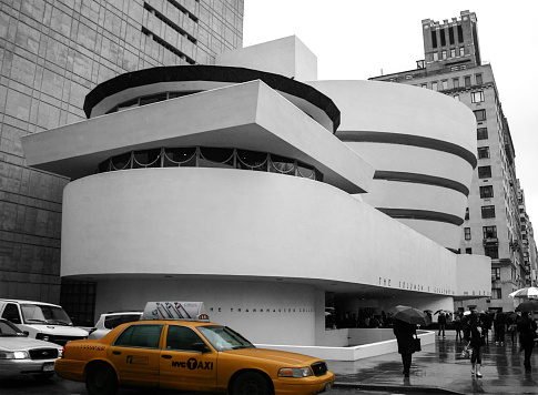 New York, NY, USA - April 04, 2011: Solomon R. Guggenheim Museum with New York taxi highlighted in colour with remaining image in black and white. Image is taken from the street corner and has people walking with umbrellas.