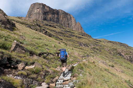 A male hiker with a blue backpack hikes along the trails in the Drakensberg Mountains near Kwazulu Natal, South Africa