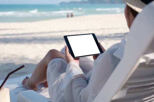 istock a woman holding a black tablet pc with blank desktop screen while laying down on beach chair 1144463714