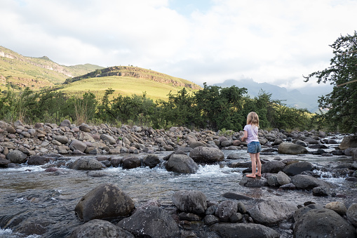 A little girl stands on the rocks in the river and enjoys playing