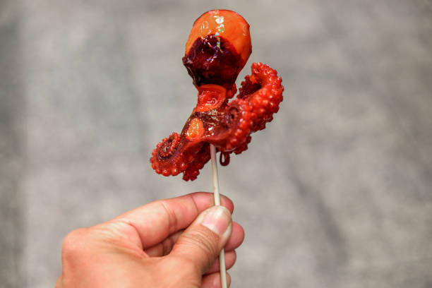 Tourist eating baby octopus in Japan street food Close up shot female hands holding a stick with marinated baby octopus takoyaki photos stock pictures, royalty-free photos & images