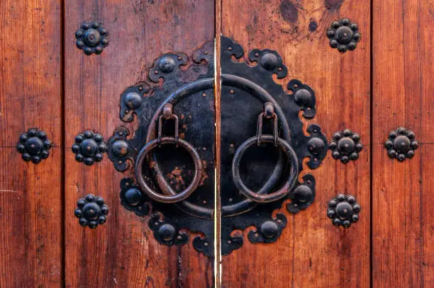 Photo of Korean wooden door panels decorated with old black metallic ring handles at a house in ancient village in Jeonju, South Korea