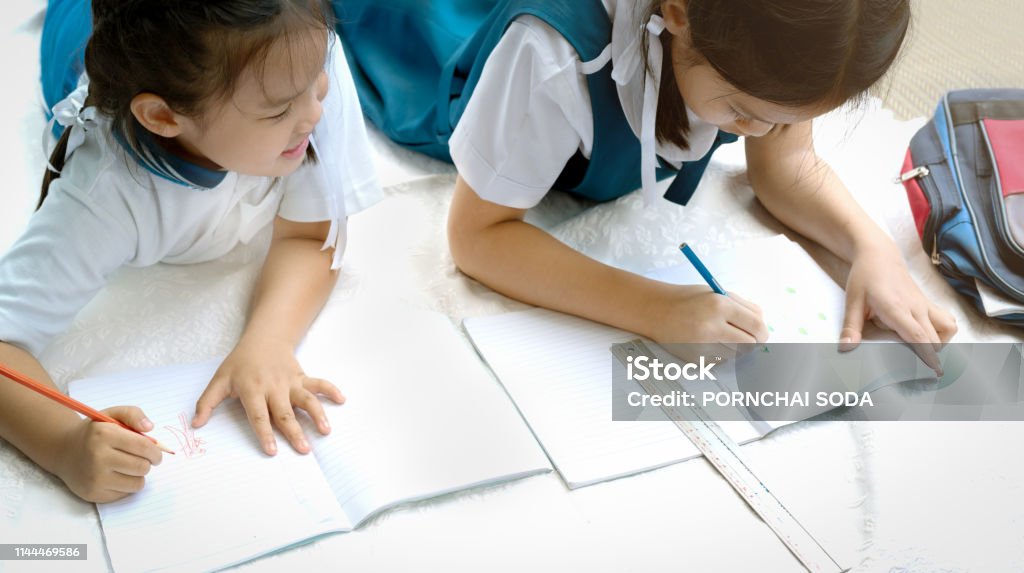 two sister girl writes a book. The decision of lessons. girl lay down drawing the picture Child Stock Photo