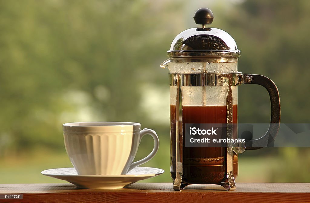 Morning Coffee at the Lake A coffee press and coffee cup shot in the morning light with a lake in the background. French Press Stock Photo