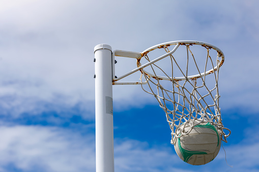 Netball and netball hoop against a blue and cloudy sky