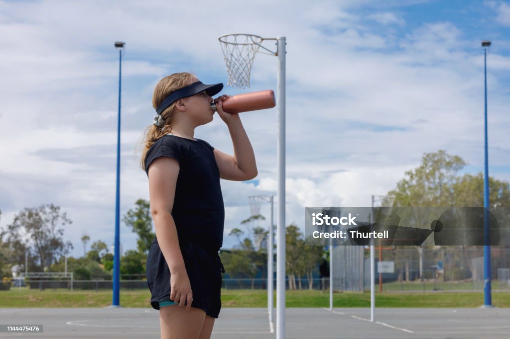 Young Girl Drinking Water After Netball Practice Young Girl Drinking Water After Netball Practice on suburban Australian netball court Netball Stock Photo