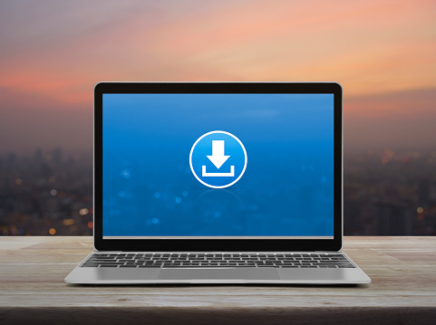 Download flat icon with modern laptop computer on wooden table over blur of cityscape on warm light sundown, Business internet online concept