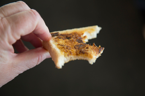 Fingers holding  toast with bites out of it, yeast spread.