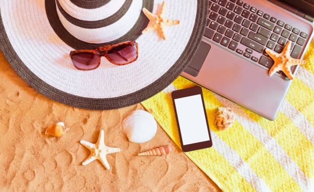 istock Laptop and smart phone with beach items on sand beach. 1144480787