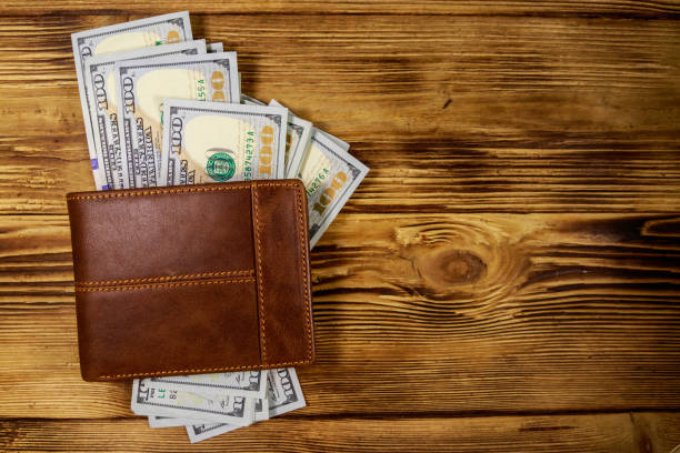 istock Brown leather wallet and american dollars on wooden table. Top view 1144483583