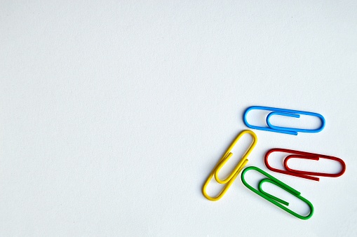 A horizontal photograph of four office paper clips over white background . Objects to the bottom right. Copy space to the left.