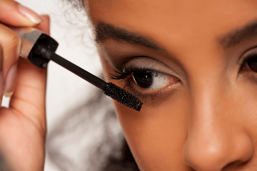 portrait of a young dark-skinned woman applying mascara on a white background