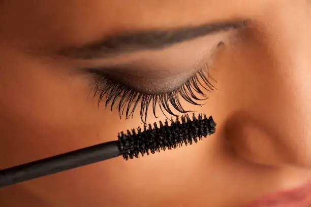 closeup of a young dark-skinned woman applying mascara on a white background