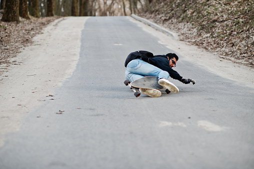 Fail falling from a skateboard. Street style arab man in eyeglasses with longboard longboarding down the road.