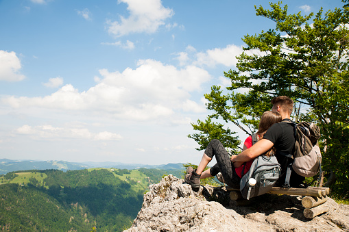 active couple rests on a mountain peak looking on a mountain landscape