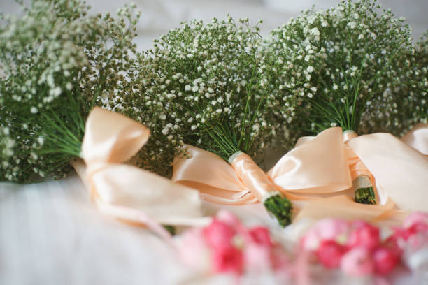 Shot during a wedding procession, this image shows the bride and bridesmaids holding tightly arranged pink rose bouquets. The shallow focus highlights the flowers against a blurred background of guests and ambiance lighting.