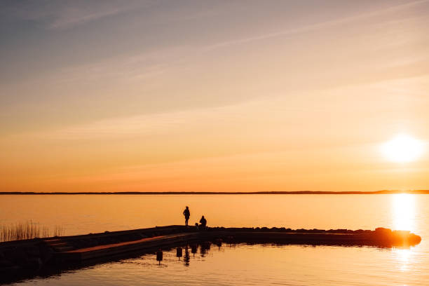 Young couple in love hugging and kissing on summer river bank at sunset. Man and woman having a romantic date