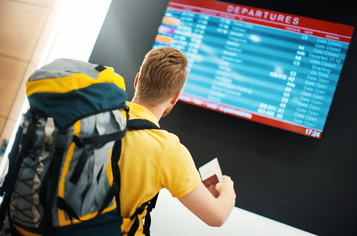 Closeup rear view of a young man with a backpack looking at arrival departure boar while waiting for his international flight.