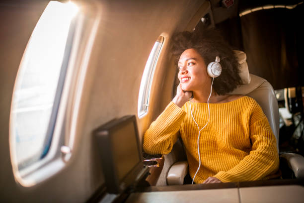 jeune femme à la mode s’asseyant sur un avion privé et regardant par une fenêtre tout en écoutant la musique par le casque - status symbol audio photos et images de collection