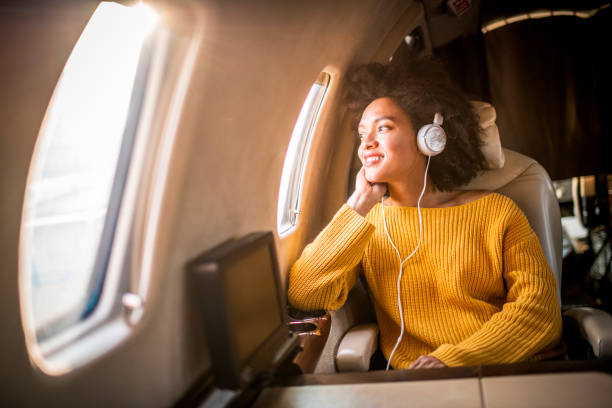 młoda modna kobieta siedząca w prywatnym samolocie i patrząca przez okno podczas słuchania muzyki przez słuchawki - high society audio zdjęcia i obrazy z banku zdjęć