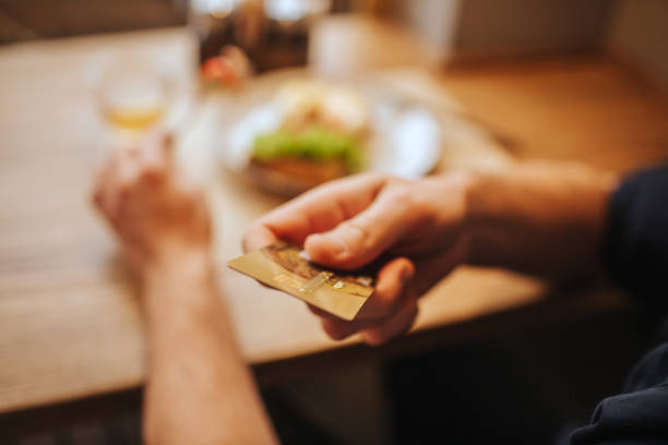 zbliżenie ręki człowieka trzymającej plastikową kartę. pokazuje go przed kamerą. facet będzie płacić za kolację. - dinner currency table business zdjęcia i obrazy z banku zdjęć