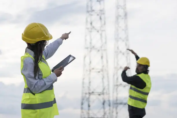 Photo of Electricity Engineers working on the field near a High Voltage Line with a Clear Blue Sky and Sun Rays behind them.