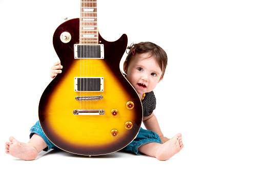 A bearded man plays the guitar and sings to a small child. Dad plays the guitar for the child. Free time for dad and baby at home. The father is on maternity leave.