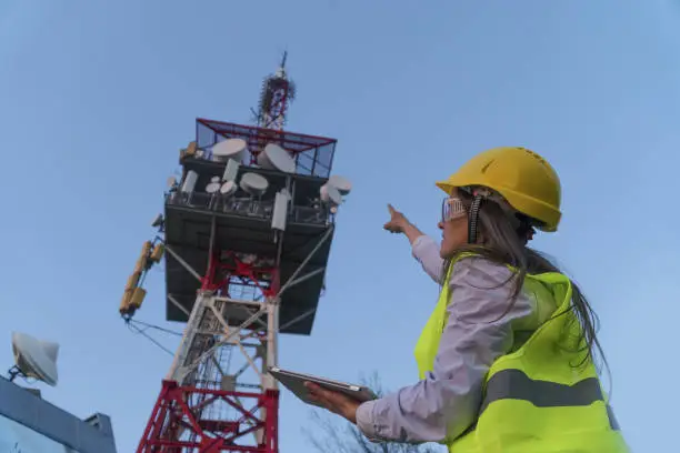Photo of Engineer working on the field near a Telecomunications tower with a Clear Blue Sky at sunset behind.