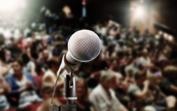 Close-up of microphone with spot lit, defocused audience Close-up of a vocal microphone seen against a spot lit, defocused  background audience. microphone stand photos stock pictures, royalty-free photos & images