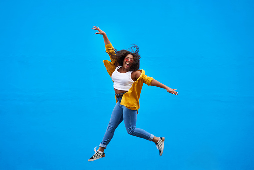 Full length shot of a happy young woman jumping into the air against a blue background