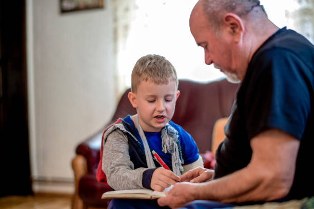 istock Little boy with broken arm doing homework with his grandfather 1144519256