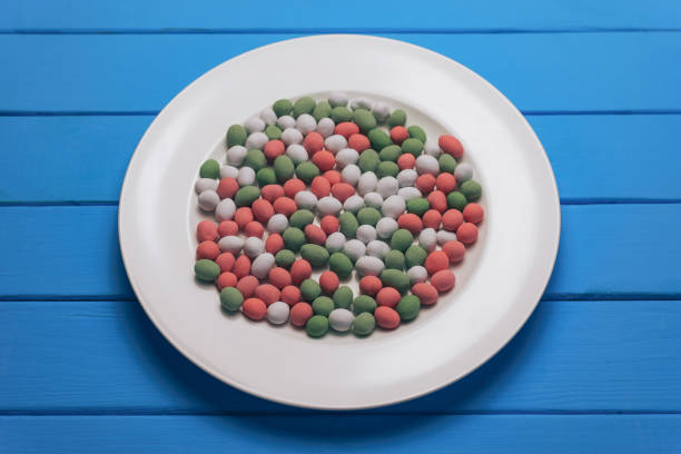 White plate with color preparations (vitamins, dyes, flavor enhancers, nutritional supplements, innovative technologies, candy sweets) on an blue wooden table background.