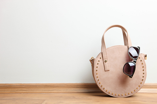 Stylish little beige round female handbag and sunglasses on wooden floor on neutral background. Concept accessory. Copy space.